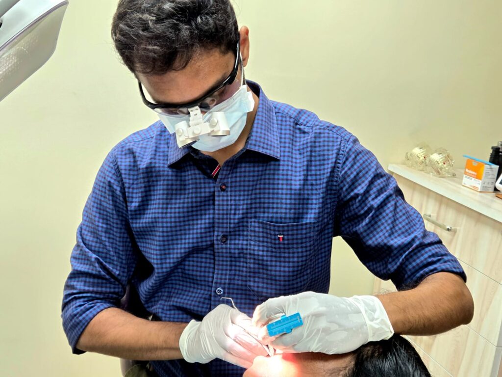 Dr. Shekar Subramanian treating a patient using dental loupes during a root canal treatment at Elegance Dental Clinic.